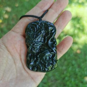 a hand holding Dark Green Jade Dragon Pendant