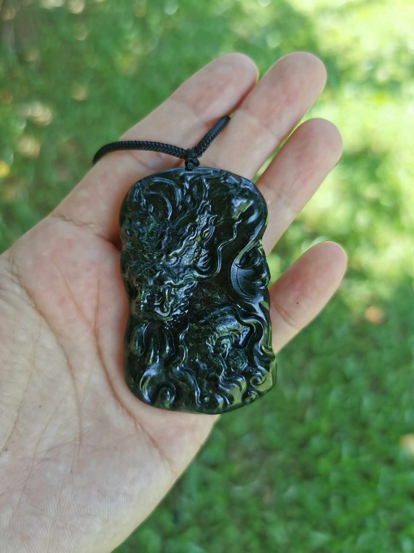 a hand holding Dark Green Jade Dragon Pendant