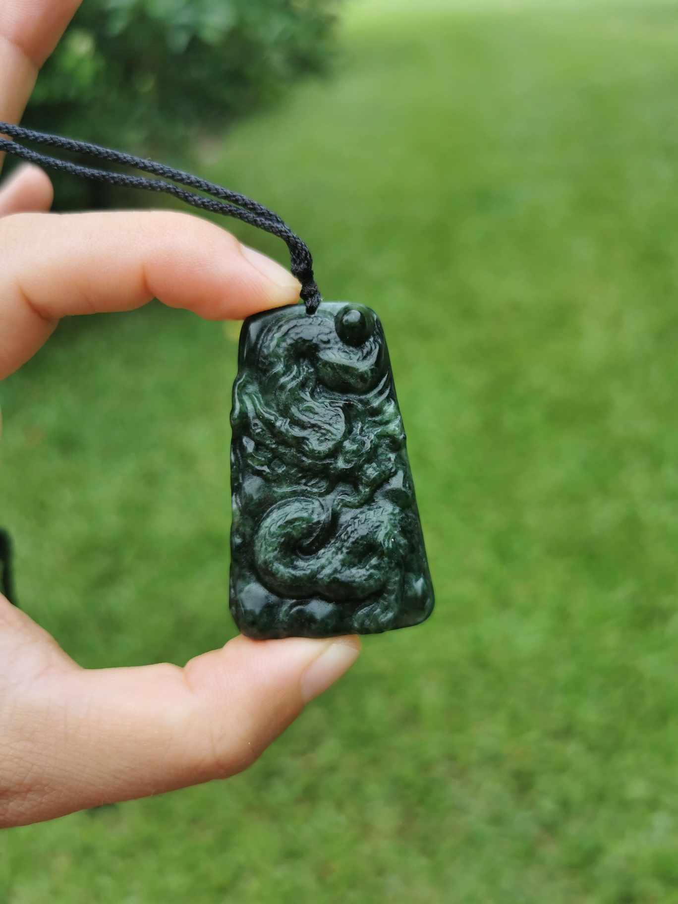 a hand holding a necklace Jade Dragon Pendant