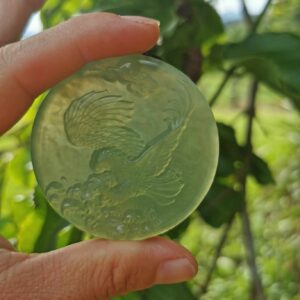 a hand holding a round jade with a bird on it